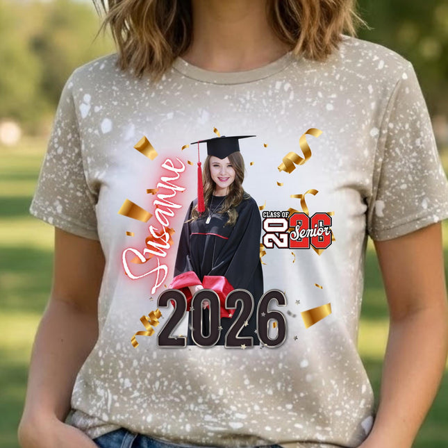 May include: A beige t-shirt with a graduation design. The design includes a photo of a graduate in a cap and gown, the name "Susanne", the year "2026", and the words "Class of 2026 Senior". Gold confetti is scattered around the design.